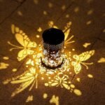 Lanterne solaire noire projetant des motifs lumineux de papillons et fleurs sur le sol en extérieur