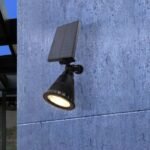 Spot LED solaire mural allumé, fixé sur un mur extérieur en béton, avec panneau solaire orienté vers le haut