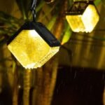 Lampe solaire suspendue allumée sous la pluie, lumière chaude, design étanche en forme de diamant