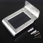 Lampe solaire LED murale en aluminium avec panneau solaire, chevilles, vis et clé d’activation sur fond noir.