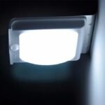 Lampe solaire murale LED allumée en pleine nuit avec détecteur de mouvement et éclairage blanc puissant.