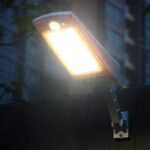 Lampe solaire LED blanche allumée sur un mur extérieur, éclairage chaud en soirée, bras articulé fixé solidement.