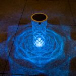 Borne solaire LED en AS projetant une lumière bleue en motif floral lumineux sur sol de terrasse la nuit
