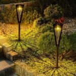 Deux lampes de jardin solaires noires diffusant une lumière chaude sur les buissons le long d’un escalier en pierre
