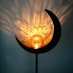 Lampe solaire lune LED avec boule en verre dorée projetant une lumière chaude et ombres décoratives.