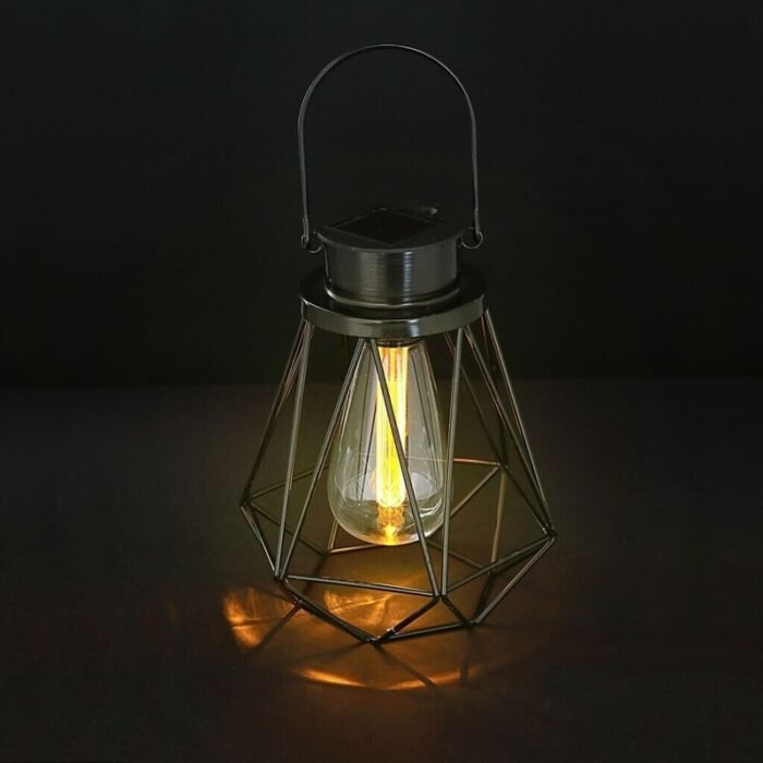 Lanterne solaire noire en métal ajouré, ampoule LED allumée diffusant une lumière chaude dans l’obscurité