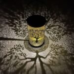 Lanterne solaire arbre de vie projetant des ombres magiques sur le sol, lumière LED chaude décorative.