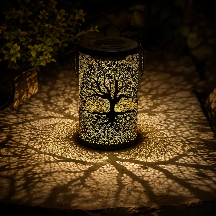 Lanterne solaire Arbre de Vie en métal ajouré projetant de grandes ombres décoratives sur une terrasse extérieure à la tombée de la nuit.