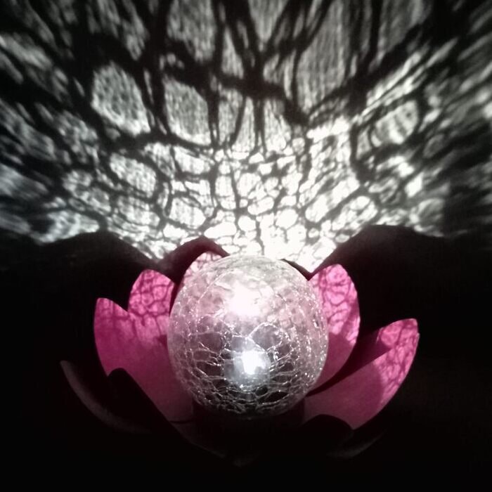 Lampe LED en forme de lotus rose projetant des ombres artistiques avec une sphère en verre craquelé.