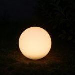 Boule lumineuse solaire LED blanche allumée, posée au sol dans un jardin de nuit, éclairage décoratif extérieur