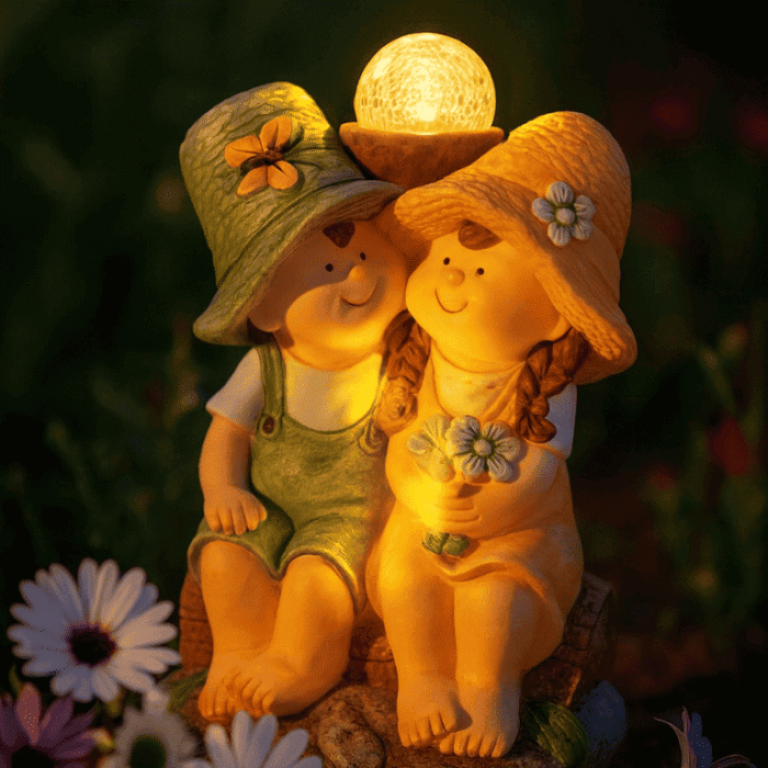 Statue solaire de jardin couple garçon et fille assis, éclairage LED blanc chaud dans un décor féérique fleuri